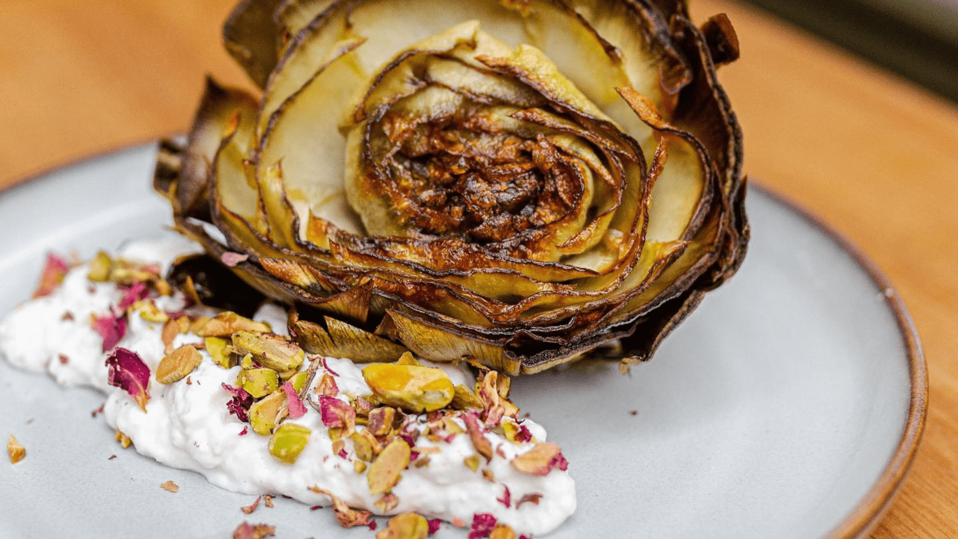 Alcachofa frita con guarnición de salsa, sobre ella frutos secos