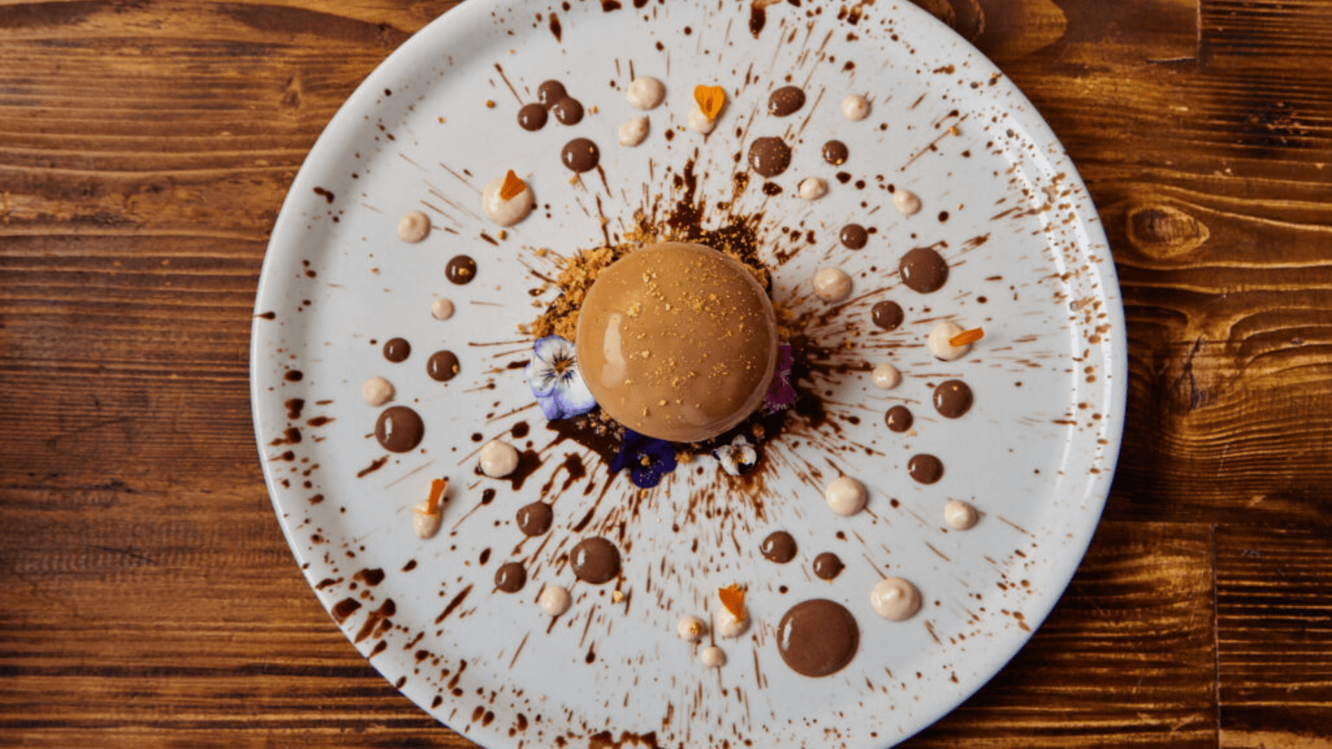 Postre de chocolate en el centro de un plato blanco decorado con salsa de chocolates sobre mesa de madera