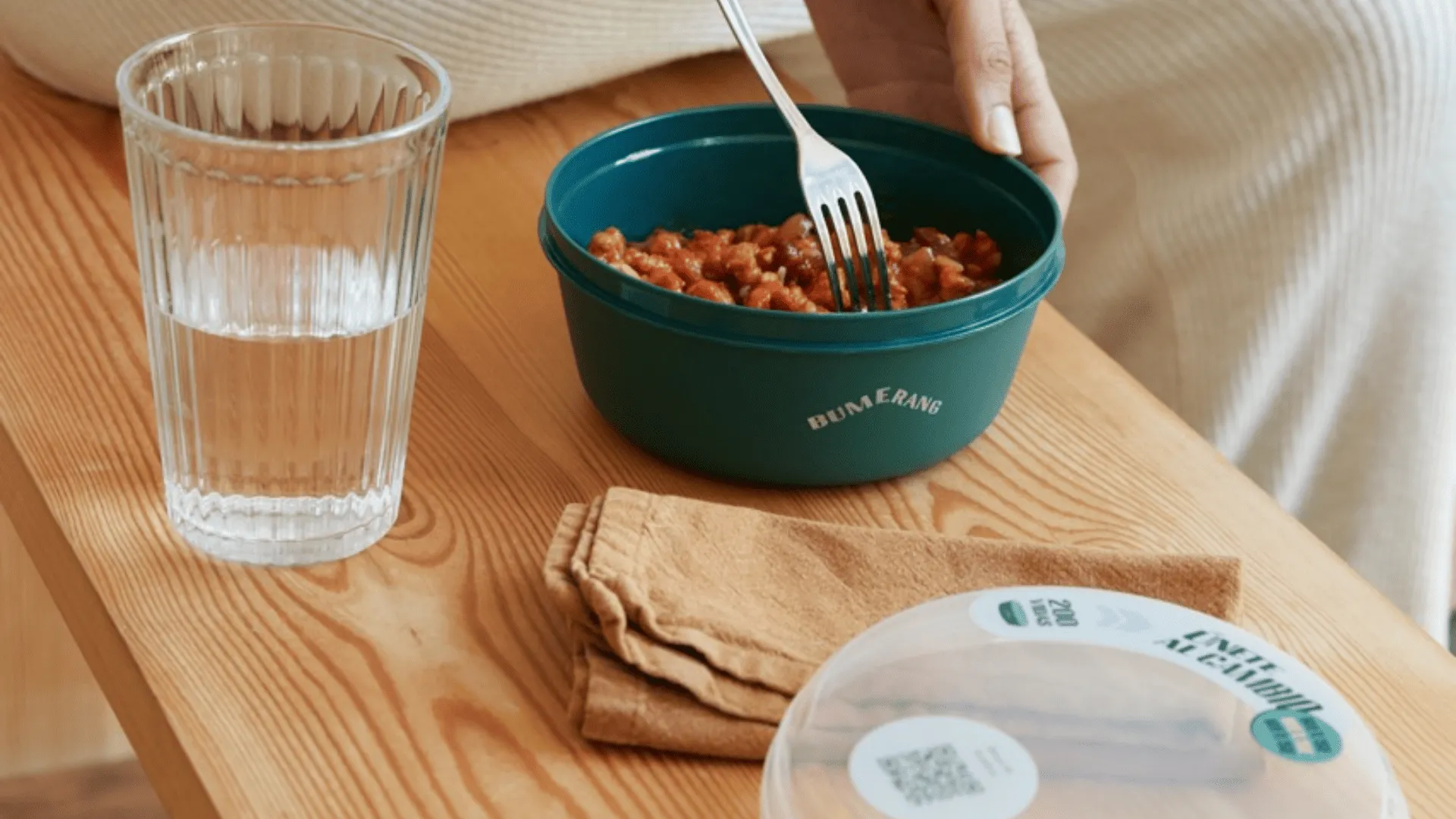 Tupper con comida sobre una mesa junto a un vaso de agua y una servilleta
